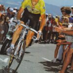 A grimacing man in a lime green jersey cycles up a mountain