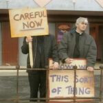 Photo showing two priests (characters in the classic 1990s comedy Father Ted) protesting with placards saying "CAREFUL NOW" and "DOWN WITH THIS SORT OF THING" outside a cinema on the fictional Craggy Island