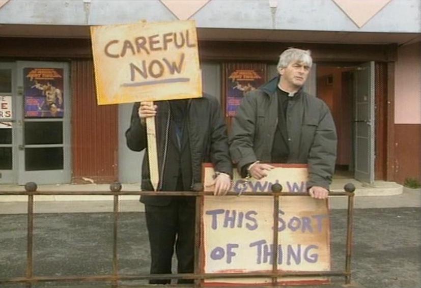 Photo showing two priests (characters in the classic 1990s comedy Father Ted) protesting with placards saying "CAREFUL NOW" and "DOWN WITH THIS SORT OF THING" outside a cinema on the fictional Craggy Island